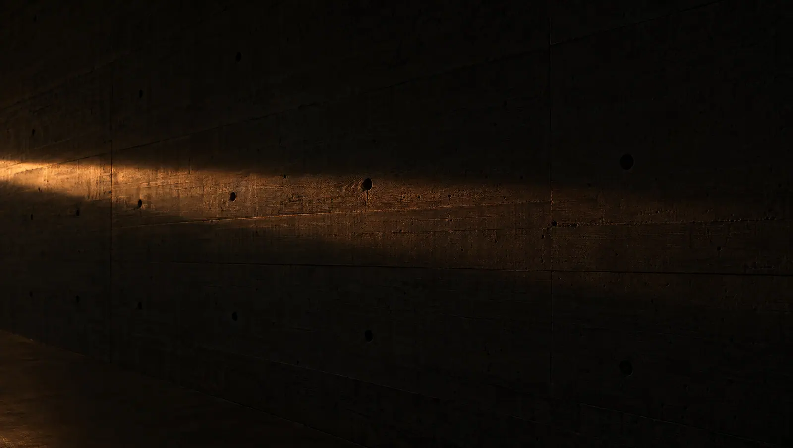 A shaft of warm light falling across a dark concrete wall