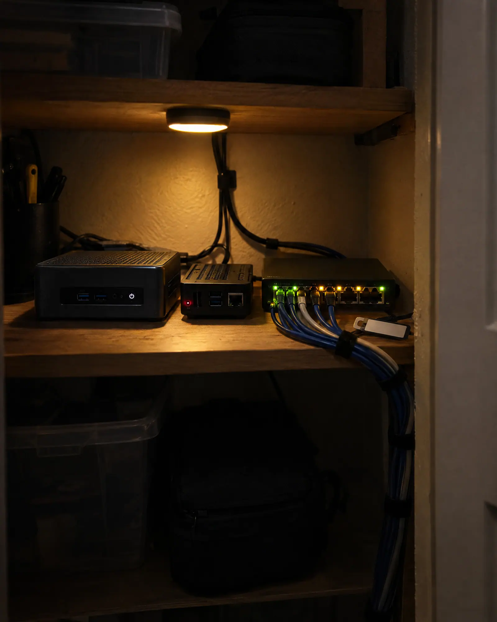 A small home lab on a closet shelf: a mini PC, a single-board computer and a network switch with blinking lights